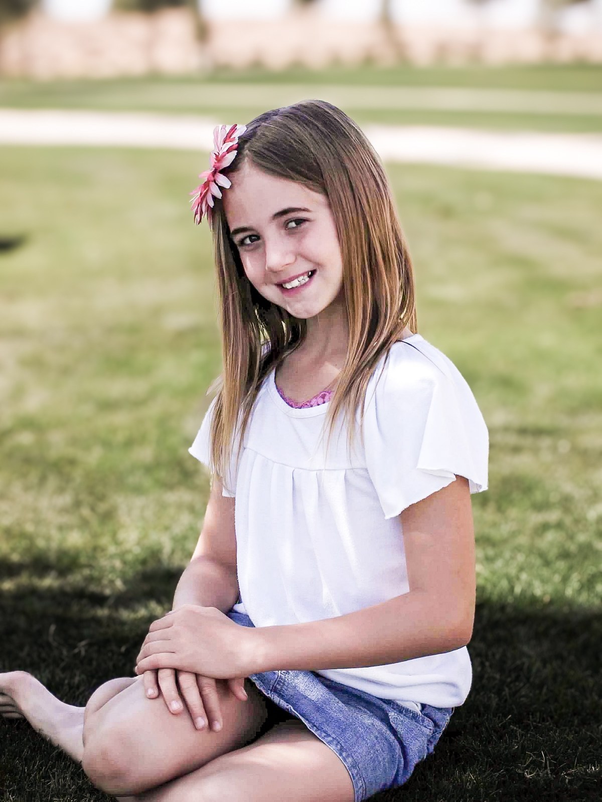 Lexi Schultz as a young girl sitting on the grass with a flower in her hair